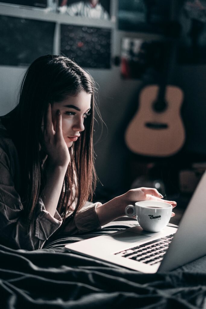 pexels-photo-4066041-4066041 Woman lying on bed, focused on laptop with a coffee cup in hand, embracing remote work lifestyle.